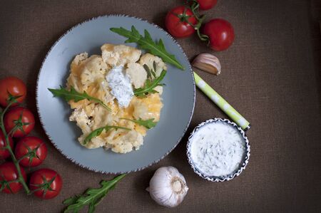 Baked cauliflower and tomatoes with cream-garlic sauce on dark brownの写真素材
