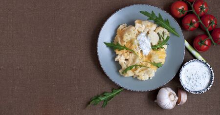 Baked cauliflower and tomatoes with cream-garlic sauce on dark brownの写真素材