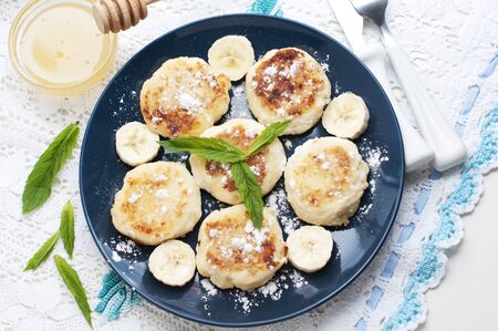 Cottage cheese pancakes, syrniki with banana and mint in blue plate. Top viewの写真素材
