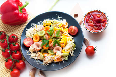 Colorful pasta with tomatoes, cheese, garlic, parsley, pepper on a black plate. Pasta for child with tomato sauce on a white background. Top viewの写真素材
