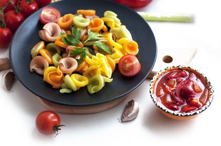 Colorful pasta with tomatoes, garlic, parsley, pepper on a black plate. Pasta for child with tomato sauce on a white backgroundの写真素材