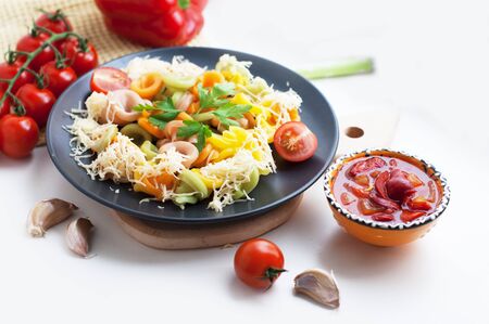 Colorful pasta with tomatoes, garlic, cheese, parsley, pepper on a black plate. Pasta for child with tomato sauce on a white backgroundの写真素材
