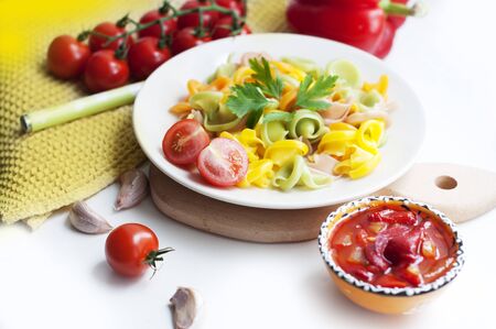Colorful pasta with tomatoes, garlic, parsley, pepper on a white plate. Pasta for child with tomato sauce on a white backgroundの写真素材