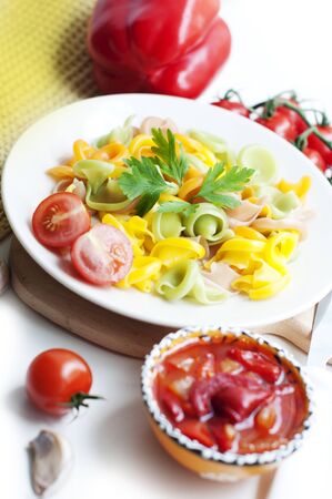 Colorful pasta with tomatoes, garlic, parsley, pepper on a white plate. Pasta for child with tomato sauce on a white backgroundの写真素材