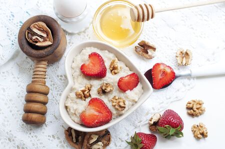 Breakfast with oatmeal with strawberries, honey, walnuts and egg on white background. Breakfast for child. Oatmeal in a white heart-shaped plate. Top viewの写真素材