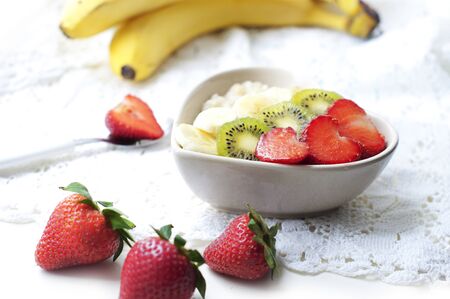 Breakfast with oatmeal with strawberries, kiwi, honey and banana on white background. Breakfast for child. Oatmeal in a white heart-shaped plateの写真素材