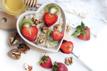 Breakfast with oatmeal with strawberries, kiwi, honey, walnuts and egg on white background. Breakfast for child. Oatmeal in a white heart-shaped bowl. Top viewの写真素材