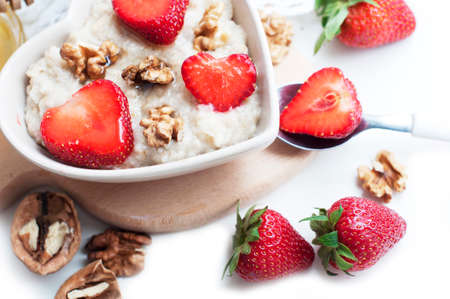 Breakfast with oatmeal with strawberries, honey, walnuts and egg on white background. Breakfast for child. Oatmeal in a white heart-shaped bowl. Top viewの写真素材
