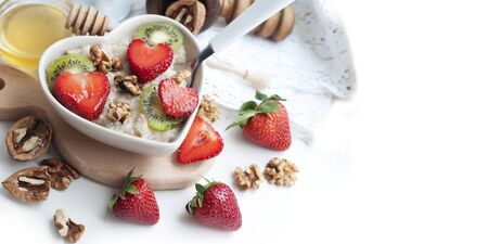Breakfast with oatmeal with strawberries, kiwi, honey, walnuts and egg on white background. Breakfast for child. Oatmeal in a white heart-shaped bowlの写真素材