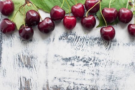 Sweet cherries with green leaves on a white wooden background. Top view
