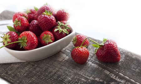 Breakfast with strawberries on wooden desk. Breakfast for child. Strawberries in a white heart-shaped bowlの写真素材