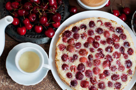 Tart with ripe sweet cherries and green tea on brown background. Homemade dessert with ripe sweet cherries. Top viewの写真素材
