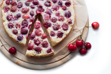 Tart with ripe sweet cherries on wooden circle board on white background. Homemade dessert with ripe sweet cherries. Top viewの写真素材