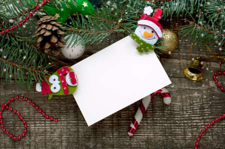 New Year and Christmas card with snowman, owl, bell, fir branches, cones and falling snow on a wooden background. A postcard with space for text on a white paper.の写真素材