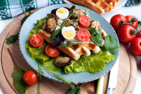 Belgian waffles with mussels, tomatoes, egg and green salad, arugula, spinach on blue plate on wooden backgroundの写真素材
