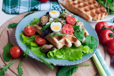 Belgian waffles with mussels, tomatoes, egg and green salad, arugula, spinach on blue plate on wooden backgroundの写真素材