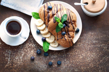 Croissant with chocolate, blueberries, bananas, and mint on a dark brown background. Breakfast with...