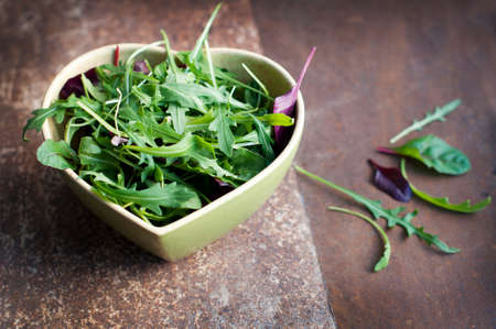 Fresh arugula, basil and spinach in a heart shaped bowl on dark brown grange backgroundの写真素材