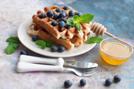 Belgian waffles with blueberries, honey and mint on a white plate. Knife and fork with white handlesの写真素材