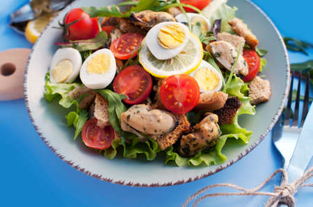 Salad with mussels, tomatoes, eggs, arugula, spinach, lemon and croutons on blue background. Seafood salad with vine sauceの写真素材