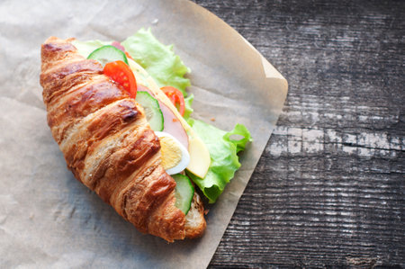 Croissant sandwich with ham, cheese, fresh salad, tomatoes, eggs and cucumber on woodenの写真素材
