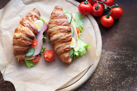 Croissant sandwiches with ham, cheese, fresh salad, tomatoes, eggs and cucumber on wooden circle board.の写真素材