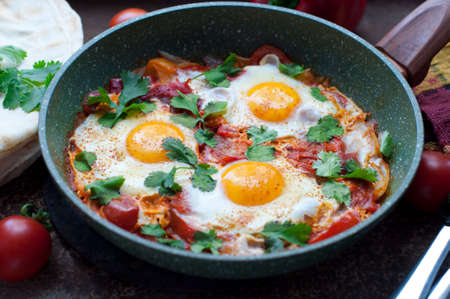 Traditional dish of israeli cuisine Shakshuka. Fried eggs with tomatoes, peppers, onions, cilantro...