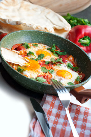 Traditional dish of israeli cuisine Shakshuka. Fried eggs with tomatoes, peppers, onions, cilantro and pita in a pan on white backgroundの写真素材