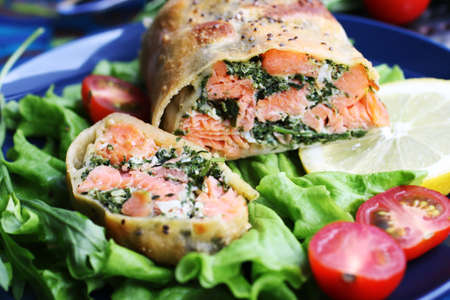 Strudel with salmon, spinach, cheese, arugula, lemon and tomatoes on blue backgroundの写真素材