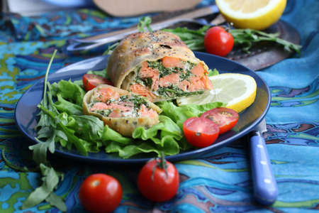Strudel with salmon, spinach, cheese, arugula, lemon and tomatoes on blue backgroundの写真素材