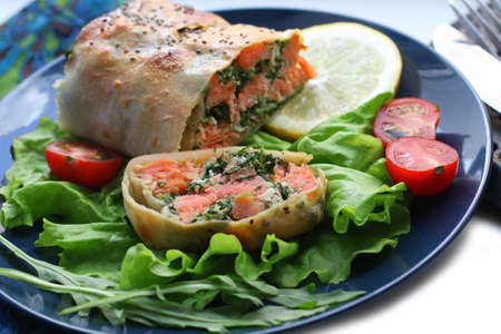 Strudel with salmon, spinach, cheese, arugula, lemon and tomatoes on blue backgroundの写真素材