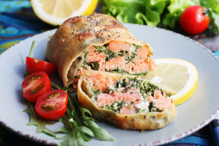 Strudel with salmon, spinach, cheese, arugula, lemon and tomatoes on blue backgroundの写真素材