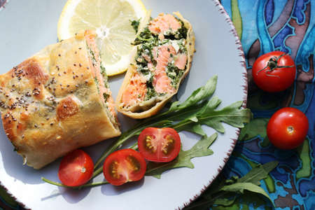 Strudel with salmon, spinach, cheese, arugula, lemon and tomatoes on blue background. Top viewの写真素材