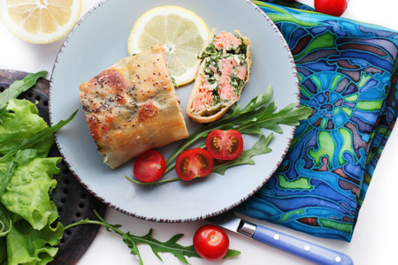 Strudel with salmon, spinach, cheese, arugula, lemon and tomatoes on white background. Top viewの写真素材