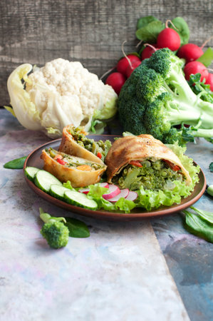 Strudel with broccoli, spinach, carrot, cauliflower and knife on brown plate on gray backgroundの写真素材
