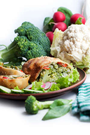 Strudel with broccoli, spinach, carrot, cauliflower and knife on brown plate on white backgroundの写真素材