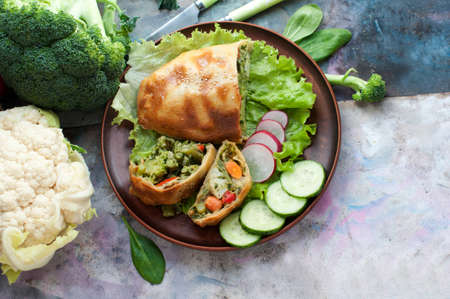 Strudel with broccoli, spinach, carrot, cauliflower and knife on brown plate on gray background. Top viewの写真素材