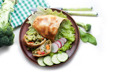 Strudel with broccoli, spinach, carrot, cauliflower and knife on brown plate on white background. Top viewの写真素材