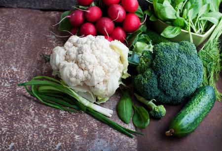 Fresh ripe vegetables on dark brown background. Spinach, radishes, green onion, cucumbers, broccoli, cauliflower, dill on rustic backgroundの写真素材