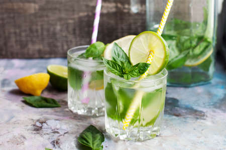 Glasses of basil lemonade with mint, basil, lime, lemon and ice on light gray backgroundの写真素材