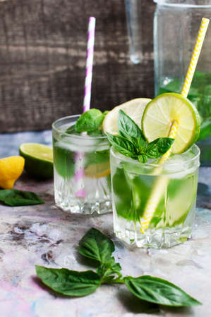Glasses of basil lemonade with mint, basil, lime, lemon and ice on light gray backgroundの写真素材