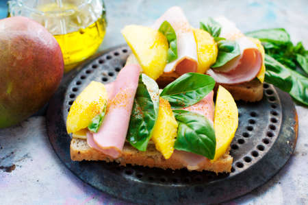 Sandwiches with mango, ham, cream cheese, basil and olive oil on a metal round trayの写真素材