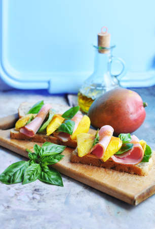 Sandwiches with mango, ham, cream cheese, basil and olive oil on a wooden boardの写真素材