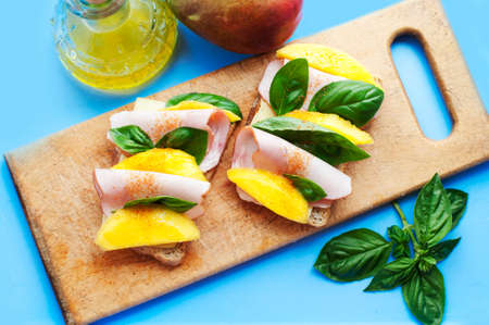 Sandwiches with mango, ham, cream cheese, basil and olive oil on a wooden boardの写真素材