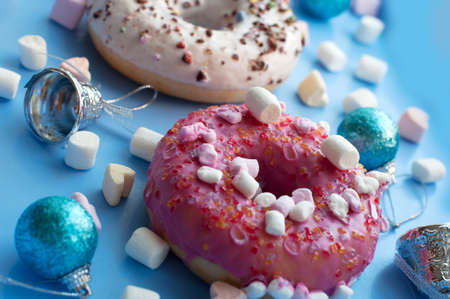 Christmas breakfast with white and pink donuts, coffee and marshmallows with Christmas decorations on blue backgroundの写真素材