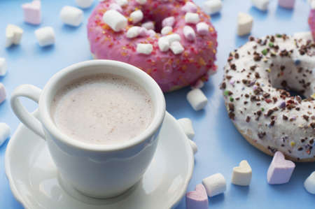 Pink and white donuts, cup of cocoa marshmallows in the shape of heart on blue backgroundの写真素材
