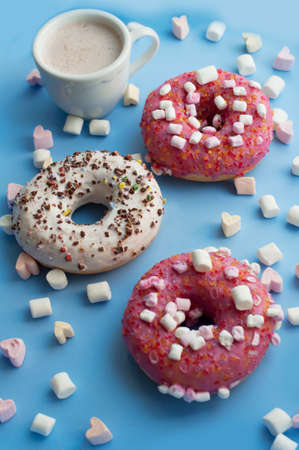 Pink and white donuts, cup of cocoa marshmallows in the shape of heart on blue backgroundの写真素材