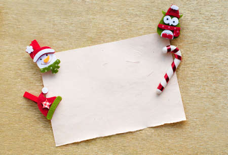 Christmas and New Year card with white paper and Christmas decorations on gold background. Snowman, owl and Santa hat on golden shine background. Place for textの写真素材