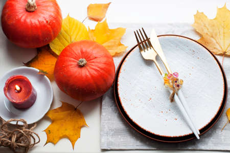 Autumn style table setting with pumpkins, yellow leaves, white plate and gold knife, gold fork, gold spoon. Top viewの写真素材