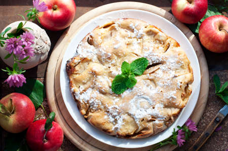 Apple homemade pie with red apples, mint and vase of flowers on wooden backgroundの写真素材